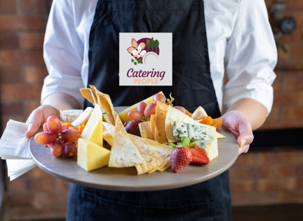 A cheese platter is being held by a waiter wearing an apron. 