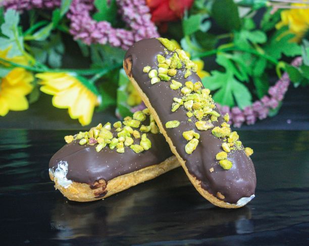 Eclair filled with whipped cream topped with dark chocolate and crushed pistachio (v)